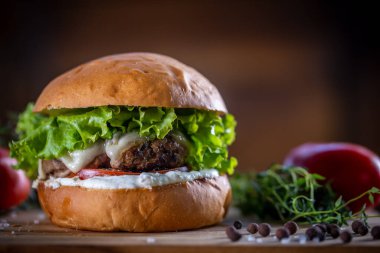 Peynirli sığır burger, marul, domates ve ahşap zemin üzerinde sos.