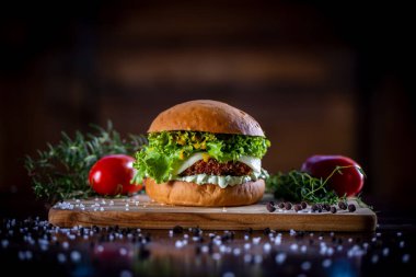 Peynirli çıtır tavuk burger, marul, domates ve ahşap zemin üzerinde sos.