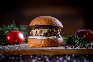 Peynirli sığır burger, ahşap arka planda karamelize soğan ve sos.