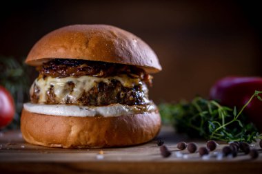 Peynirli sığır burger, ahşap arka planda karamelize soğan ve sos.