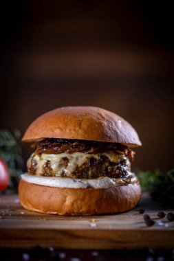Peynirli sığır burger, ahşap arka planda karamelize soğan ve sos.