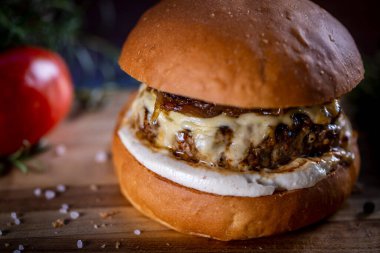Peynirli sığır burger, ahşap arka planda karamelize soğan ve sos.