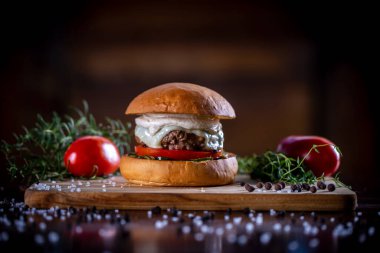 Peynirli sığır burger, domates, turşu ve ahşap arka planda sos.