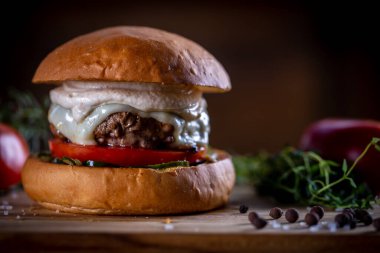 Peynirli sığır burger, domates, turşu ve ahşap arka planda sos.