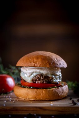 Peynirli sığır burger, domates, turşu ve ahşap arka planda sos.