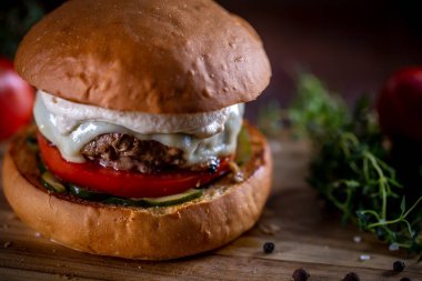 Peynirli sığır burger, domates, turşu ve ahşap arka planda sos.