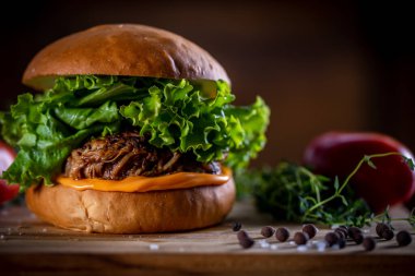 Çedarlı domuz sandviçi, marul ve ahşap arka planda mor soğan.