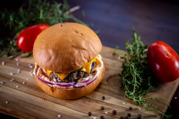 Çedarlı sığır burger, pastırma, turşu, mor soğan ve ahşap zemin üzerinde sos.