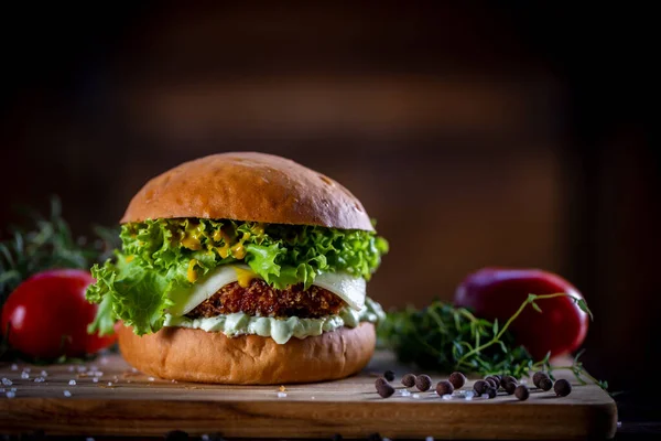 Craft crispy chicken burger with cheese, lettuce, tomato and sauce on wooden background