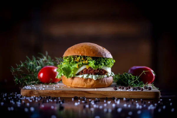 Craft crispy chicken burger with cheese, lettuce, tomato and sauce on wooden background