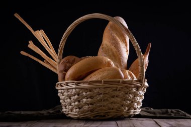 Koyu arkaplandaki ahşap masada sepetteki ekmek çeşitleri. Fırın Çeşitliliği.