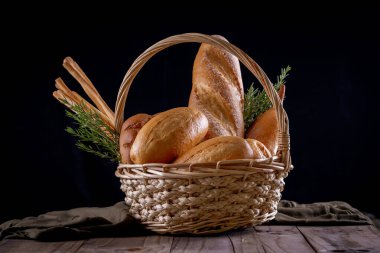 Koyu arkaplandaki ahşap masada sepetteki ekmek çeşitleri. Fırın Çeşitliliği.