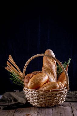 Koyu arkaplandaki ahşap masada sepetteki ekmek çeşitleri. Fırın Çeşitliliği.