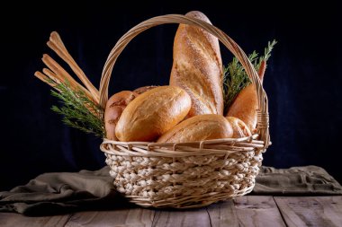 Koyu arkaplandaki ahşap masada sepetteki ekmek çeşitleri. Fırın Çeşitliliği.
