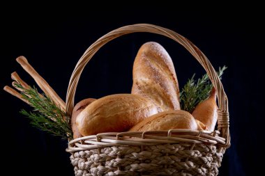 Koyu arkaplandaki ahşap masada sepetteki ekmek çeşitleri. Fırın Çeşitliliği.