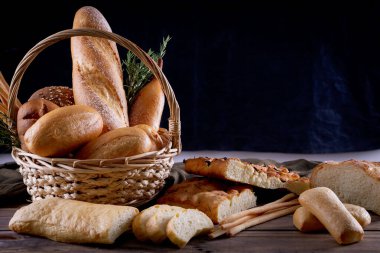 Koyu arkaplandaki ahşap masada sepetteki ekmek çeşitleri. Fırın Çeşitliliği.