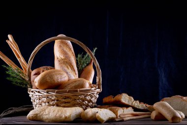 Koyu arkaplandaki ahşap masada sepetteki ekmek çeşitleri. Fırın Çeşitliliği.
