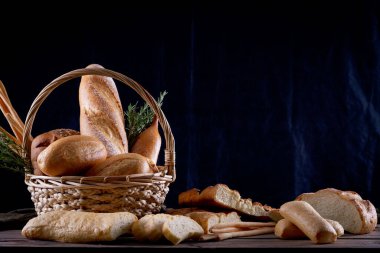 Koyu arkaplandaki ahşap masada sepetteki ekmek çeşitleri. Fırın Çeşitliliği.