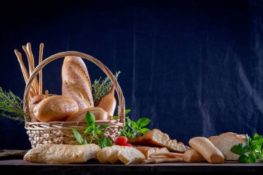 Koyu arkaplandaki ahşap masada sepetteki ekmek çeşitleri. Fırın Çeşitliliği.