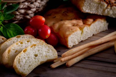 Koyu arkaplandaki ahşap masada sepetteki ekmek çeşitleri. Fırın Çeşitliliği.