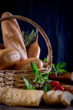 Koyu arkaplandaki ahşap masada sepetteki ekmek çeşitleri. Fırın Çeşitliliği.