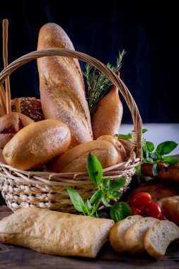 Koyu arkaplandaki ahşap masada sepetteki ekmek çeşitleri. Fırın Çeşitliliği.