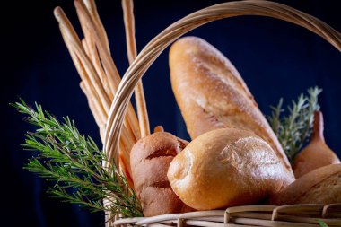 Koyu arkaplandaki ahşap masada sepetteki ekmek çeşitleri. Fırın Çeşitliliği.