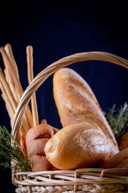 Koyu arkaplandaki ahşap masada sepetteki ekmek çeşitleri. Fırın Çeşitliliği.