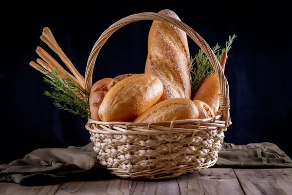 Koyu arkaplandaki ahşap masada sepetteki ekmek çeşitleri. Fırın Çeşitliliği.