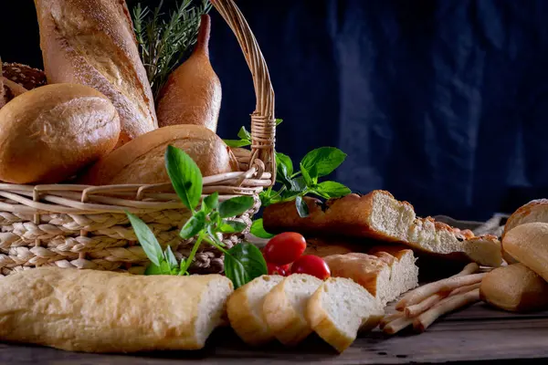 Koyu arkaplandaki ahşap masada sepetteki ekmek çeşitleri. Fırın Çeşitliliği.