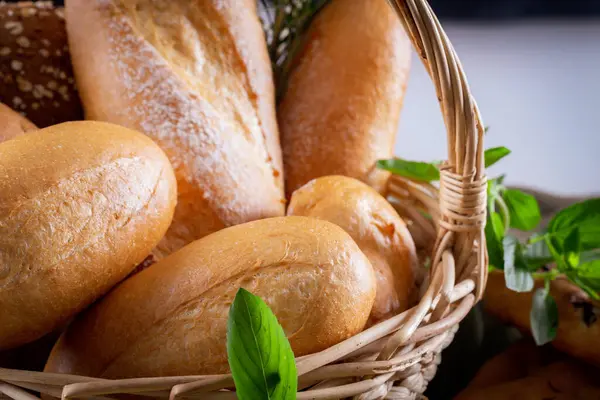 Koyu arkaplandaki ahşap masada sepetteki ekmek çeşitleri. Fırın Çeşitliliği.