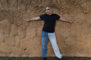 Sokakta duvara yaslanırken Güney Amerikalı olmayan genç biri başka tarafa bakıyor. LGBTIQ ve etnik çeşitlilik. Kopyalama alanı ile.