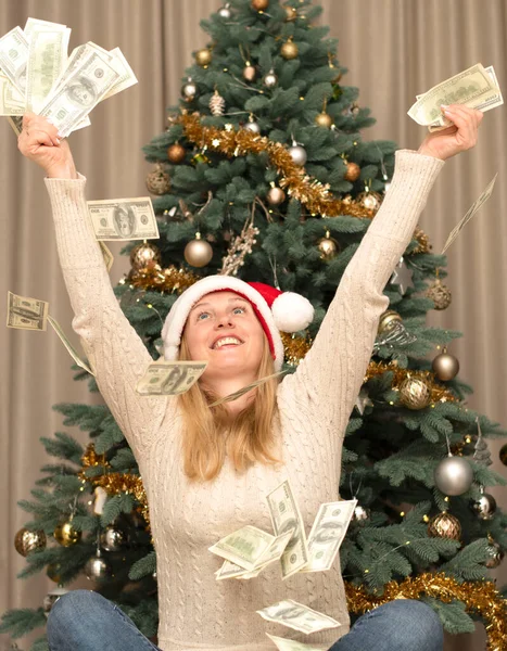 Holiday. A beautiful girl in a red santa claus hat throws up and catches paper money on the background of a Christmas tree. Flying money. Concept. Black Friday.