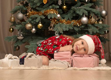 Noel konsepti. 2023. Noel Baba şapkası ve kırmızı yeni yıl elbisesi giymiş güzel beyaz kız Noel ağacının altında hediyelerle kutuları kucaklıyor..