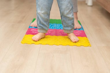 Health concept. Two boys stand barefoot on a colorful orthopedic massage mat in a home interior. Massage and improve blood circulation in the legs. Close-up of children's legs.