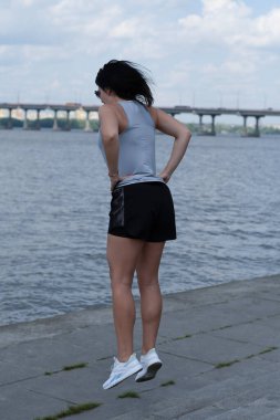 İnce ve uzun boylu bir kız nehrin kenarındaki setin üzerindeki basamaklara atlar. Açık hava sporları. Bacak egzersizi. Fitness konsepti.