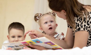 Aile kavramı. Kitap okuyorum. Anne, oğul ve kız kitap okuyarak ve evde boş zaman geçirerek eğleniyorlar. Evde çocuklara ders vermek. Yakın plan. Yumuşak odak.