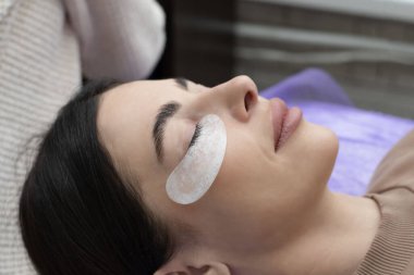 Güzellik konsepti. Kozmetoloji. Kirpik uzantıları. Güzeller güzeli bir kız güzellik salonundaki kanepede yatıyor. Bir uzman, bir uzman kirpikleri kirpiklerini uzatıyor. Yakın plan..