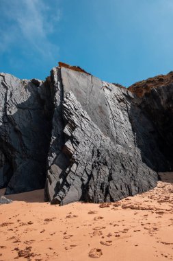 Huzurlu bir sahil, kayalık bir çıkıntı, ve yumuşak kum, sahil doğasının dingin güzelliğini yakalıyor..