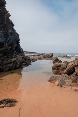 A tranquil beach, a rocky outcrop, and the soft sand, capturing the serene beauty of coastal nature. clipart