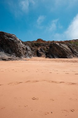 A tranquil beach, a rocky outcrop, and the soft sand, capturing the serene beauty of coastal nature. clipart