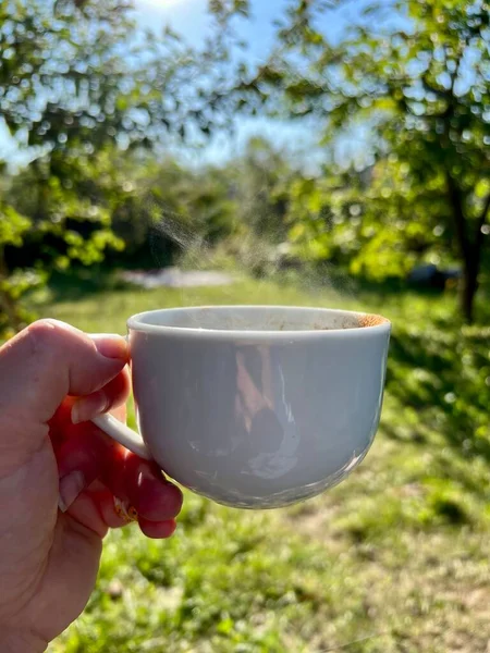 Bir fincan kahveyle kadın eli, yakın plan çay, bahçe. Dikey fotoğraf, sabah konsepti. Yüksek kalite fotoğraf