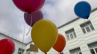Bulutlu bir gökyüzünde yüzen renkli balonlar ve beyaz bir bina