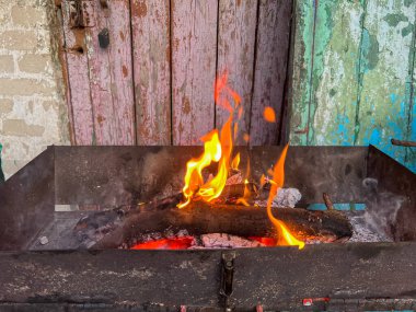 Yıpranmış ahşap bir kapının zeminine kurulmuş tahta odunlarla yanan ateş.