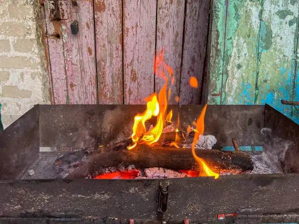 Yıpranmış ahşap bir kapının zeminine kurulmuş tahta odunlarla yanan ateş.