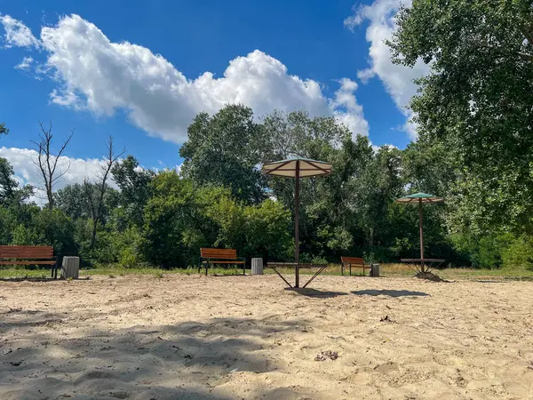 Tahta banklar ve güneş gözlüğü altındaki piknik masaları ziyaretçileri yemyeşil ağaçlarla çevrili kumlu bir sahilde dinlenmeye davet ediyor.