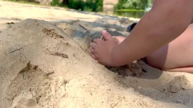 Güneşli bir sahilde kumdan kale yapan bir çocuk.