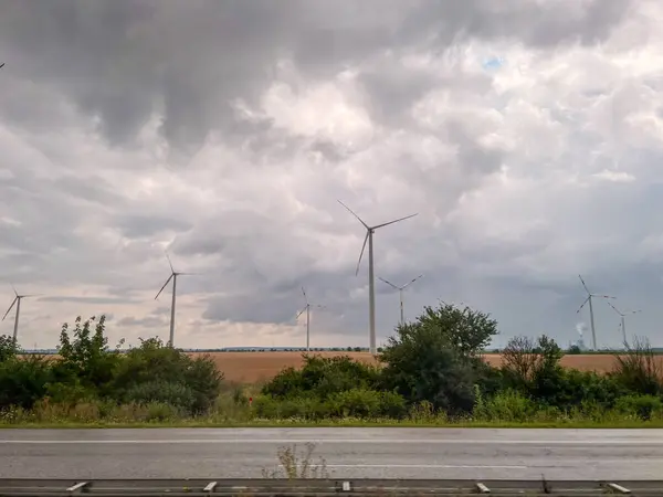 Rüzgâr türbinleri bulutlu bir gökyüzünün altındaki otobanın yanındaki alanda temiz enerji üretiyor.