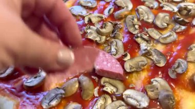 Şef pizza üzerine sosis, domates ve mantar ekliyor.