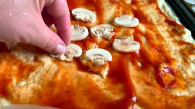 Şef domates soslu pizza hamuruna mantar ekliyor.